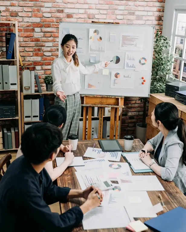 A professional training three users on the ServiceNow platform, using a whiteboard with charts for visual guidance.