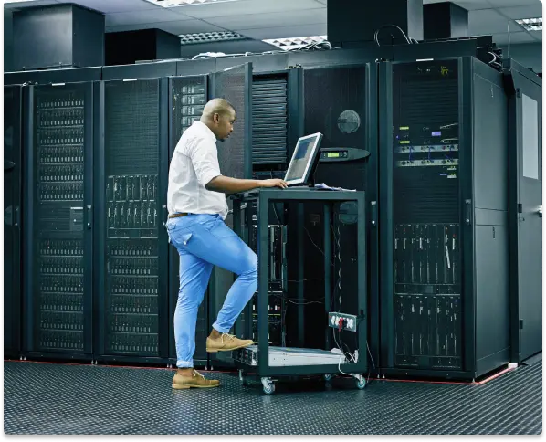 The maintenance personnel are in front of the data server racks, carrying out scheduled maintenance of data center assets using a laptop.