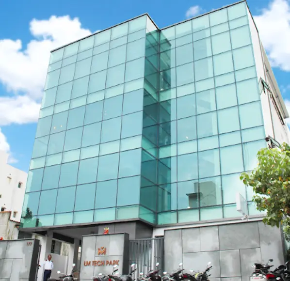 Modern office building with a glass facade labeled 'LM Tech Park.' Motorcycles are parked in front, and the building stands tall against a blue sky with clouds.