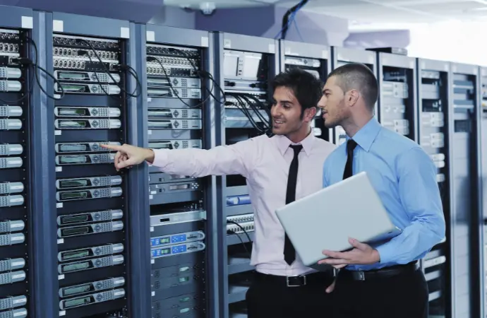 Two men discussing data management in front of servers in a ServiceNow ITOM data center.